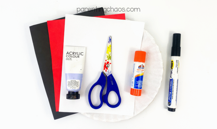 Craft supplies for a vampire paper plate craft: black, red, and white construction paper, purple acrylic paint, preschool scissors, glue stick, black marker, and a paper plate.