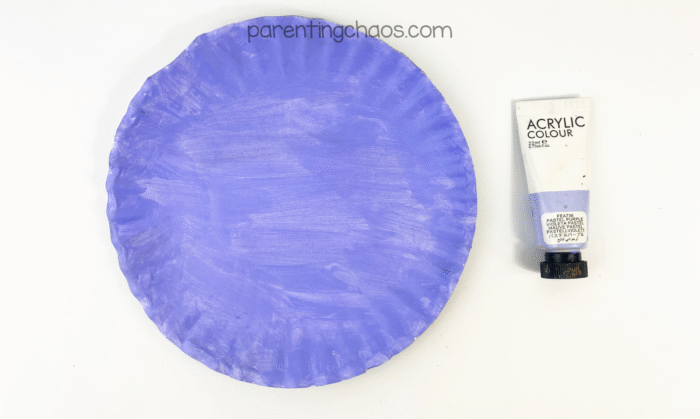 Paper plate painted purple with a tube of purple acrylic paint beside it.