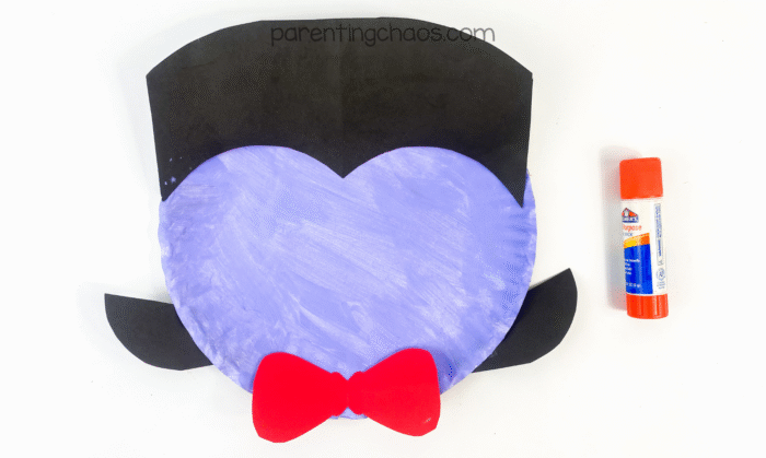 Purple paper plate with black hair and ears glued on top, and a red bow tie at the bottom.