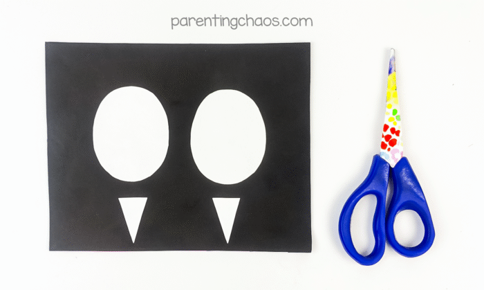 Black construction paper with two white oval eyes and two triangle shapes cut out.