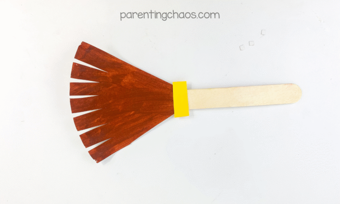 Finished witch broom paper plate craft on white background.