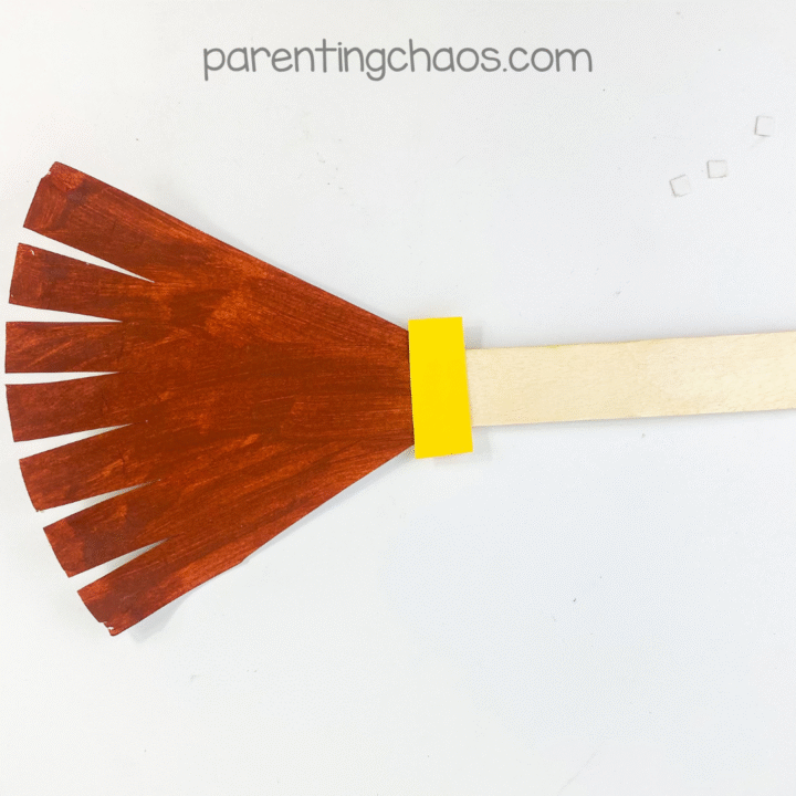 Finished witch broom paper plate craft on white background.