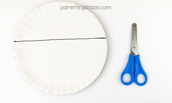 Paper plate with a horizontal cut line drawn across the center beside a pair of blue scissors.