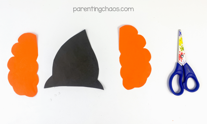 Cut-out witch hat and orange hair pieces made from construction paper beside scissors.