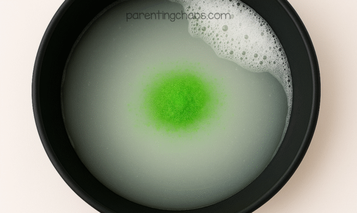 Green powder added to soapy water in a black tray, starting to mix and bubble.