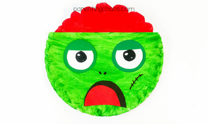 Finished paper plate zombie craft with bright green face and red brain.