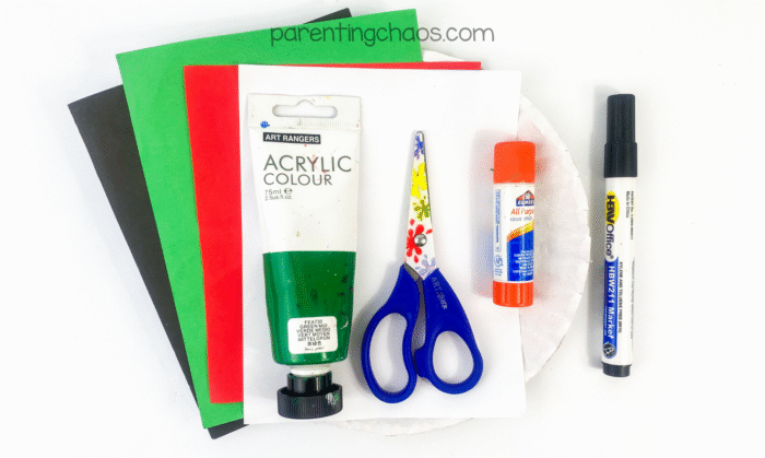 Craft supplies for paper plate zombie craft — green acrylic paint, construction paper, glue stick, scissors, and marker.