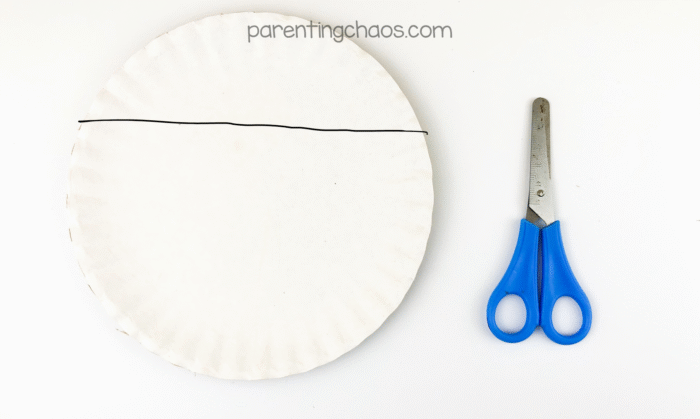 Paper plate with a line drawn across the top fourth and scissors ready to cut.