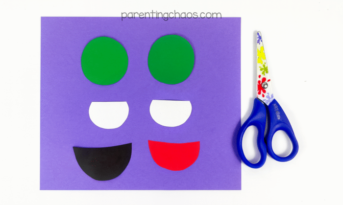 Construction paper shapes cut out for eyes and mouth on purple background.