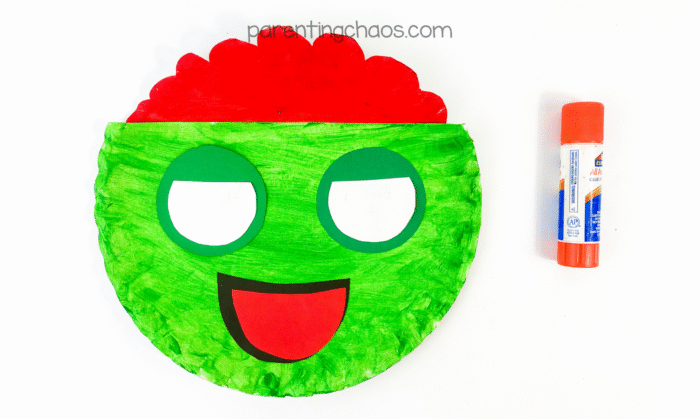Paper plate zombie face assembled with eyes and mouth glued in place.