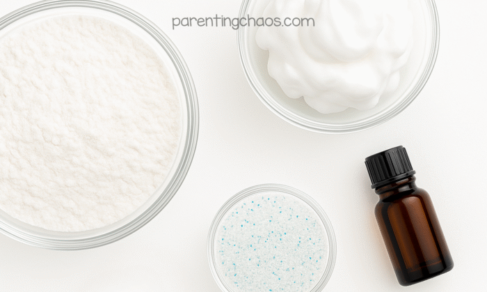 Overhead photo of four clear bowls showing the ingredients for 2 ingredient fake snow — baking soda, shaving cream, iridescent glitter, and a small amber essential oil bottle — on a white background.