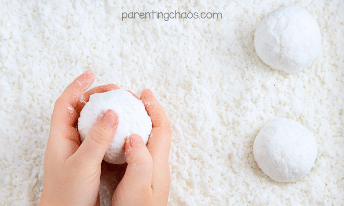 A child forming a snowball out of homemade fake snow on a soft white surface, with other snowballs resting nearby.