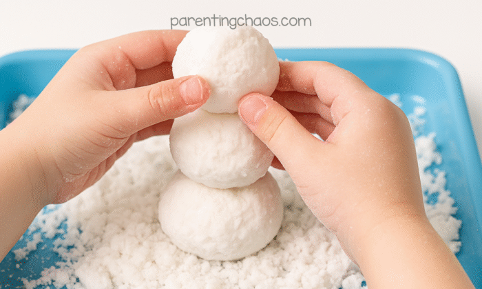A child stacking three fake snowballs in a light blue tray to build a snowman using 2 ingredient fake snow.
