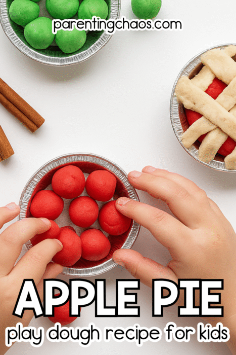 A child’s hands press red play dough balls into a small foil pie pan. Next to the child are mini pies filled with red and green play dough and a pie topped with tan lattice strips. Cinnamon sticks rest nearby. Text reads “Apple Pie Play Dough Recipe for Kids.”
