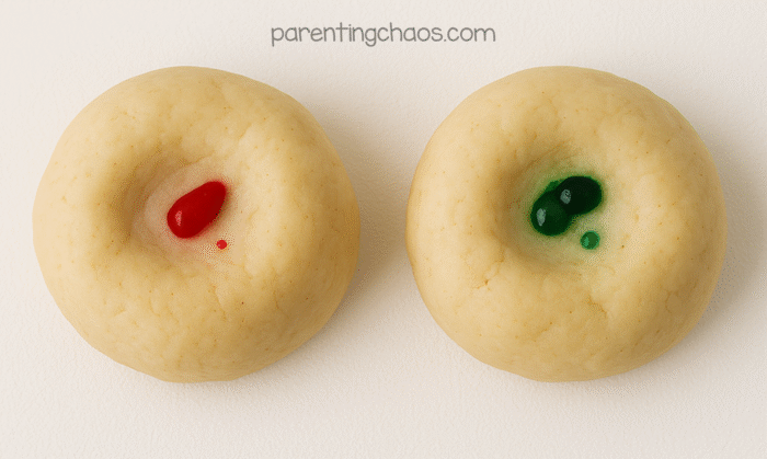 Two dough balls with red and green food coloring drops in the center, ready to be kneaded for the apple pie playdough recipe.