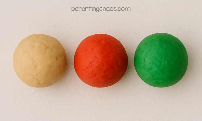 Three finished playdough balls—plain, red, and green—lined up and ready for play in this apple pie playdough recipe.