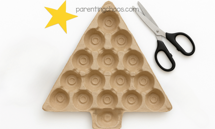 Unpainted egg carton cut into a Christmas tree shape with black scissors and a yellow paper star on a white background.