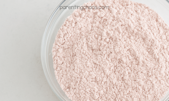 Flour and cranberry powder mixture shown in a clear bowl after being blended into a soft pink powder for moon sand.