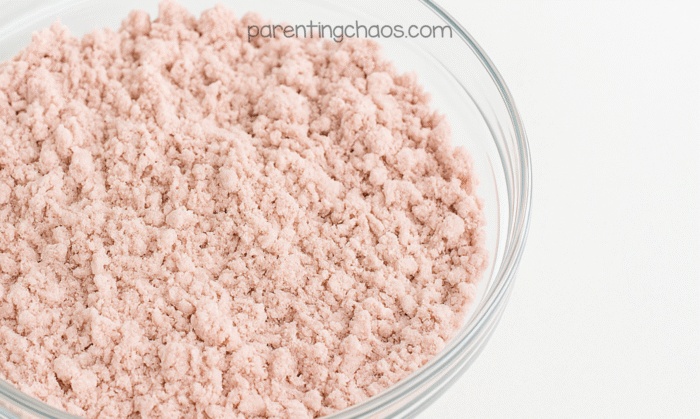 Fully mixed cranberry moon sand with a soft, crumbly texture in a clear glass bowl ready for sensory play.