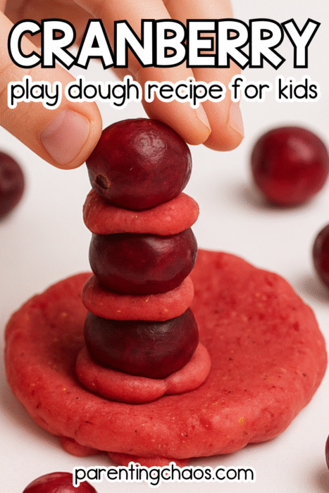 Child stacking cranberries and play dough pieces into a tall tower for a Thanksgiving-themed sensory play activity.
