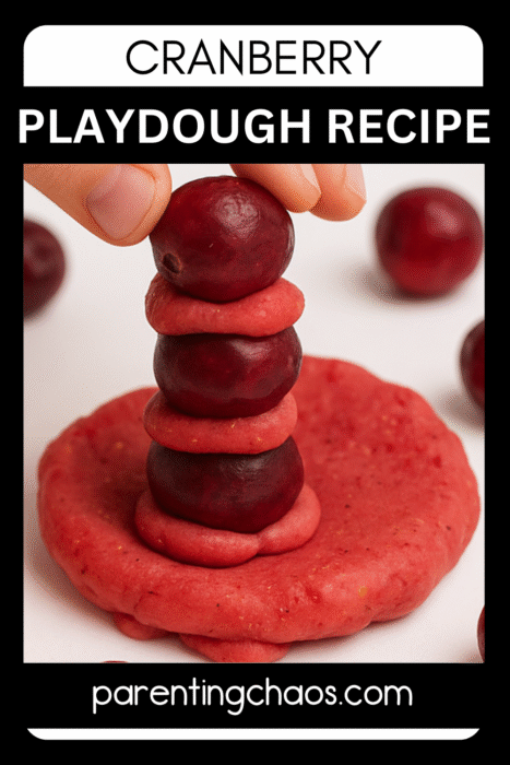 Child stacking fresh cranberries and red play dough discs in a tower for a fine motor play activity.