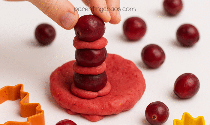 Child stacking whole cranberries and pieces of playdough into a tall tower during sensory play.