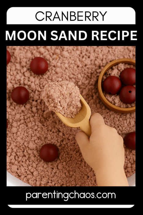 A child’s hand using a wooden scoop to lift pink cranberry moon sand from a sensory bin. Red wooden balls and a bowl of moon sand are visible. Text reads “Cranberry Moon Sand Recipe” and “parentingchaos.com.”