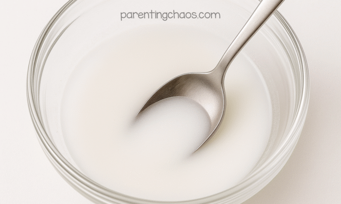 Spoon stirring the white baking soda solution in a clear glass bowl.