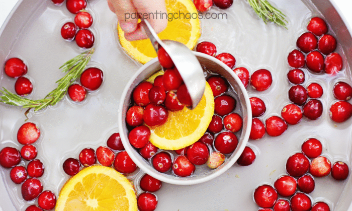 Close-up of a child using a metal ladle to scoop floating cranberries and orange slices into a bowl during cranberry water sensory play.
