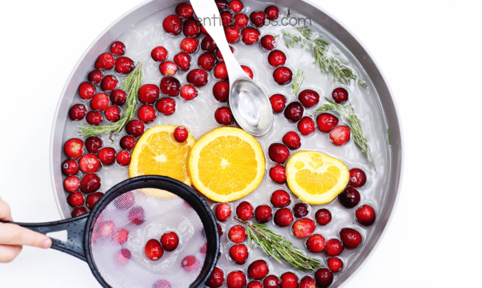 Overhead photo of a cranberry sensory bin with oranges, rosemary, and a strainer and spoon ready for scooping and pouring play.