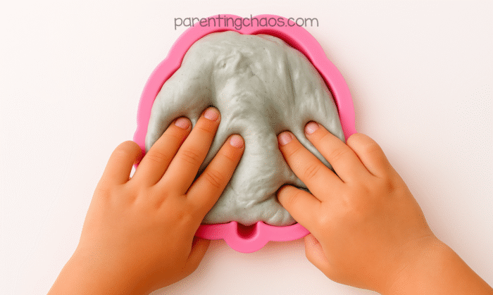 Child’s hands pressing gray slime into a pink brain mold, shaping it to fit the mold’s details.