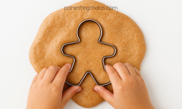 Child’s hands pressing a metal gingerbread man cookie cutter into a flattened puddle of gingerbread fluffy slime.