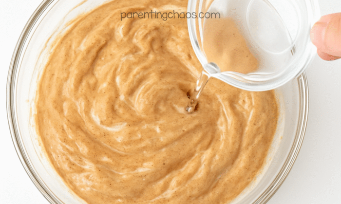 Small clear bowl of saline solution being poured into the gingerbread slime mixture.