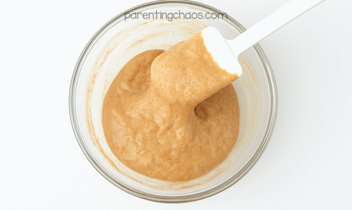 Gingerbread-colored fluffy slime starting to pull away from the sides of the bowl as it’s mixed with a white spatula.