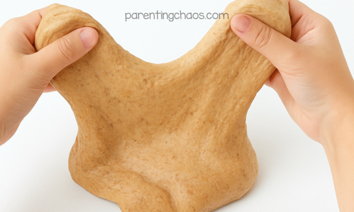 Child’s hands stretching gingerbread fluffy slime upward to show its soft, stretchy texture.