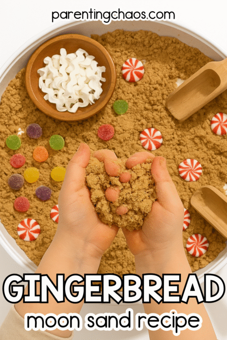 A child’s hands hold brown gingerbread moon sand shaped like a heart. The sensory bin includes red and white peppermint candies, colorful gumdrops, a wooden bowl of white ribbon pieces, and wooden scoops. Text reads “Gingerbread Moon Sand Recipe.”