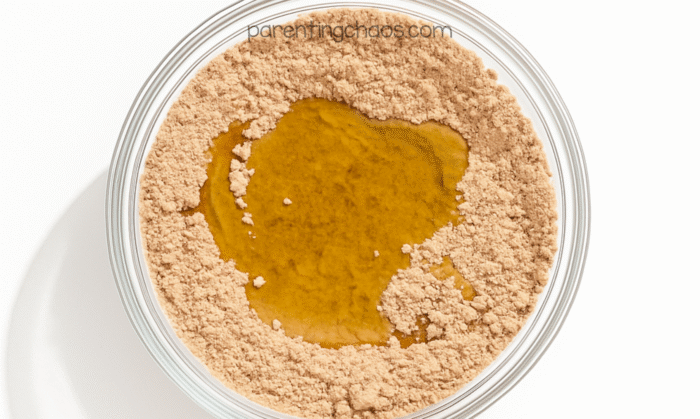Oil poured into the spiced flour mixture in a glass bowl for the moon sand recipe.