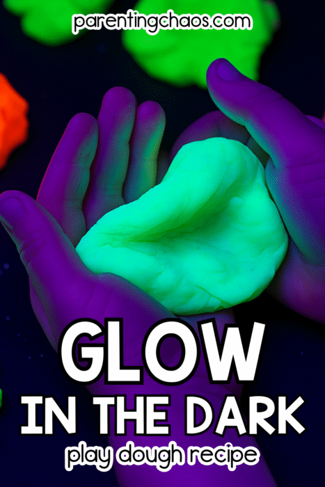 Hands holding glowing green playdough under blacklight surrounded by neon dough colors — glow in the dark play dough recipe by Parenting Chaos.