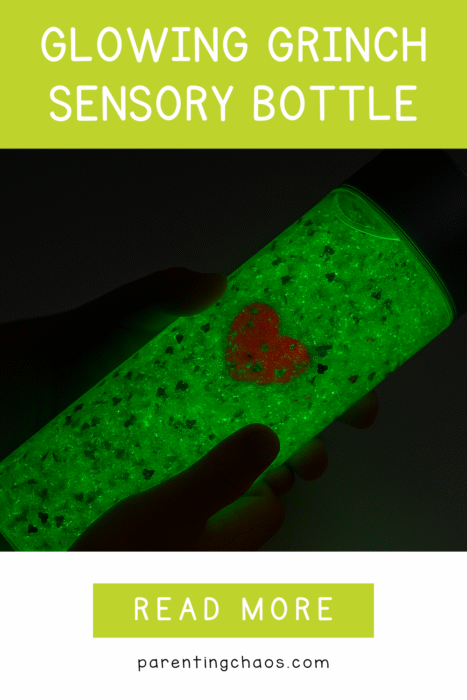Close-up of a glowing green Grinch sensory bottle held by a child, with bright green glow and red heart charm.