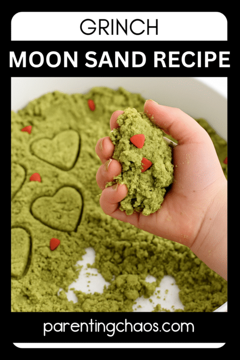 A child holding a handful of green Grinch moon sand with red heart sprinkles, with heart shapes stamped in the tray below.