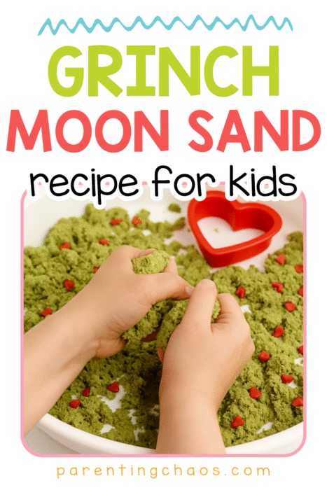 A child scooping and squeezing green Grinch moon sand with red heart sprinkles in a sensory tray.