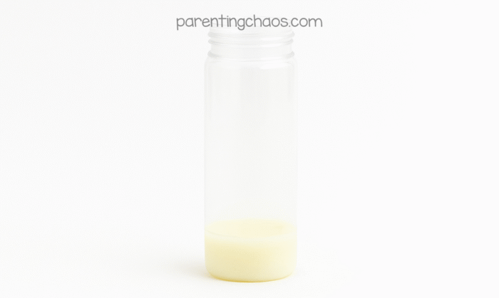 An empty clear sensory bottle sitting upright on a white background with a small layer of glow in the dark school glue pooled at the bottom.