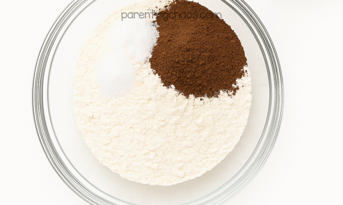 Dry ingredients for hot cocoa playdough — flour, salt, and cocoa powder — combined in a glass mixing bowl before stirring.