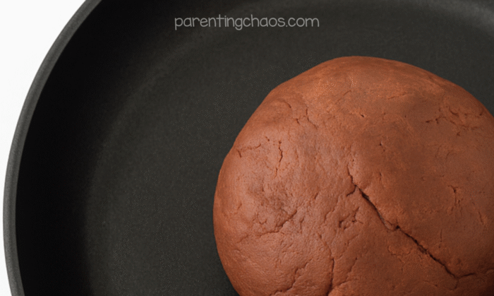 Freshly cooked ball of chocolate-colored playdough resting in a black pan after being mixed.