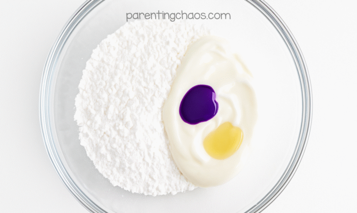 Mixing bowl with cornstarch, white conditioner, and drops of purple and yellow coloring before stirring.