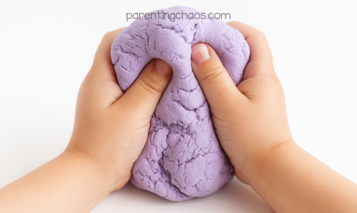 Close-up of two hands squishing soft lavender playdough, showing texture and stretch.