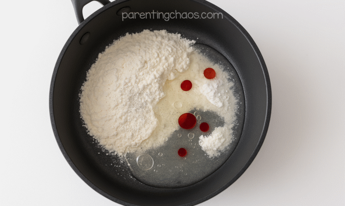Playdough mixture in a black pan with flour, water, oil, and peppermint extract before stirring together.