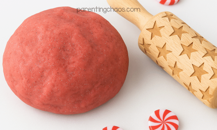 Ball of red peppermint playdough with glitter beside a star-embossed rolling pin and peppermint toy candies.