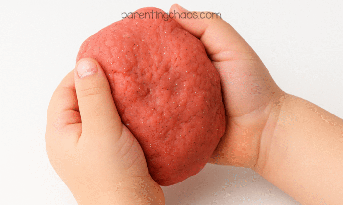 Child holding a soft ball of red peppermint playdough sprinkled with glitter.
