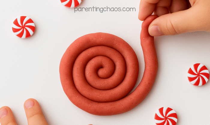 Child shaping a peppermint playdough snake into a spiral surrounded by red and white peppermint toy candies.